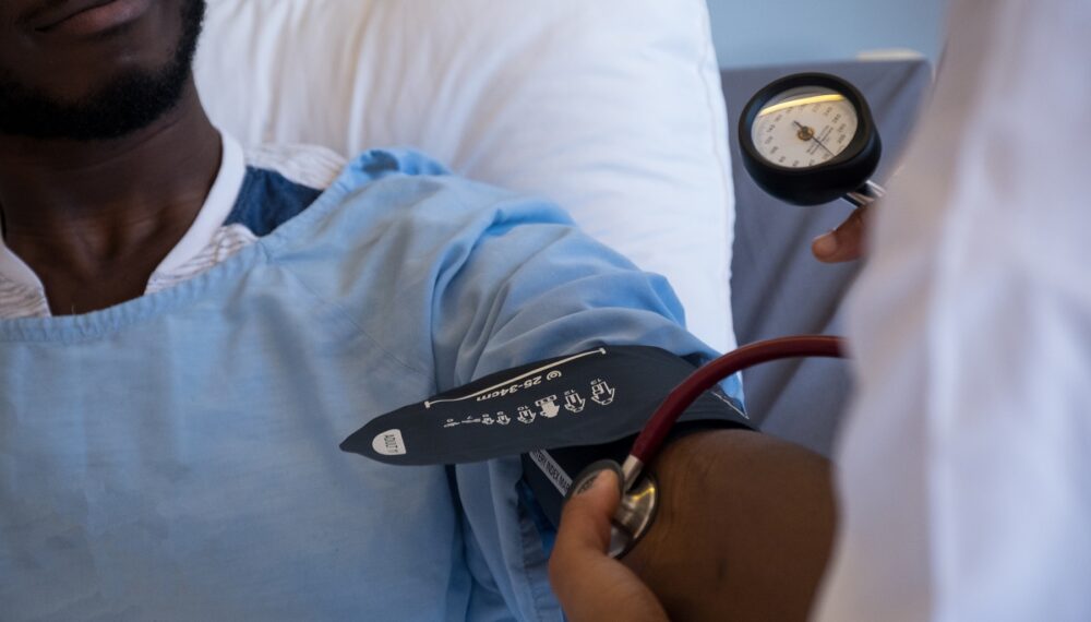 An African male patient lies in bed while the female medical doctor checks at his blood pressure